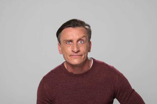 Portrait of mature man with raised eyebrow standing against grey background.