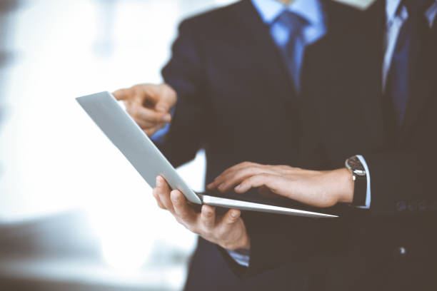 istock Business people discussing a presentation at meeting, standing in a modern office. Unknown businessman with a colleague search for some information at the laptop, lawyers at negotiation. Teamwork and partnership concept 1295964220