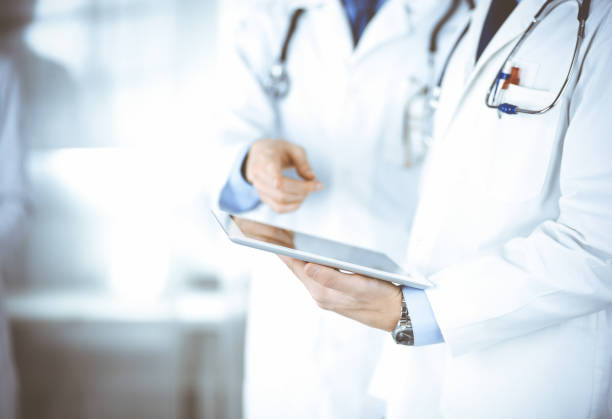 istock Group of unknown doctors use a computer tablet to check up some medical names records, while standing in a hospital office. Physicians ready to examine and help patients. Medical help, insurance in health care, best desease treatment and medicine concept 1295964540
