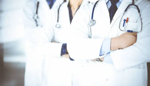 Photo of Group of modern doctors standing as a team with crossed arms and stethoscopes in hospital office. Physicians ready to examine and help patients. Medical help, insurance in health care, best desease treatment and medicine concept