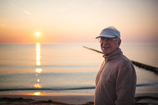 Friendly senior with sun hat and glasses is smiling in the camera by the beautiful Baltic Sea on Hiddensee in sunset