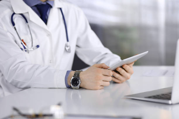 istock Unknown male doctor sitting and working with tablet computer in clinic at his working place, close-up. Young physician at work. Perfect medical service, medicine concept 1295966621