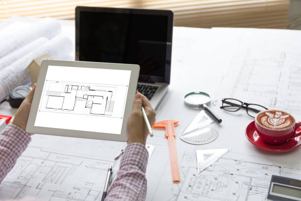 istock Architect hands  working with tablet. Architectural project, blueprints, ruler, dividers, laptop and engineering tools on working  desk. 1295966628