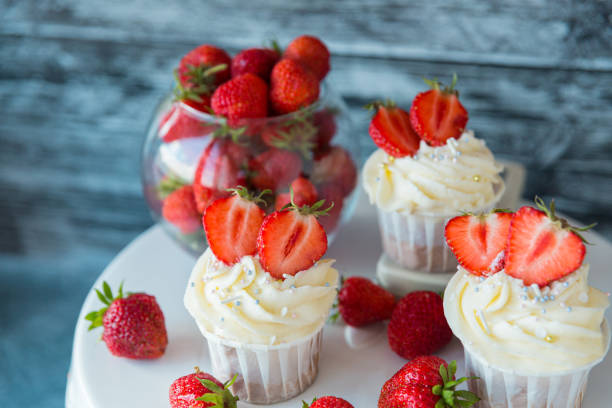istock Delicious cupcakes with white cream decorated with strawberries on a gray background. 1295966789