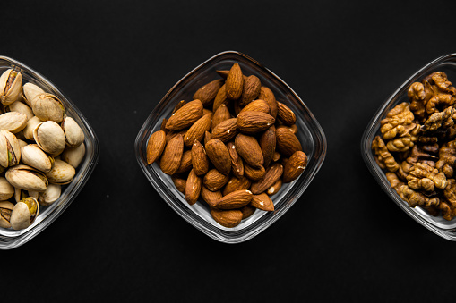 Almond, pistachio and walnut in a small plates which standing on a black table. Nuts is a healthy vegetarian protein and nutritious food