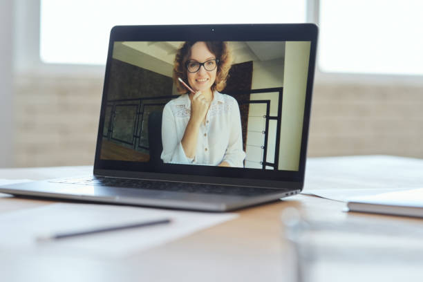 istock Cheerful female teacher smiling at camera during video call, having online lesson with schoolchildren studying from home. Focus on laptop screen 1295968272