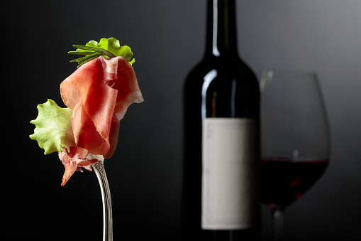 Prosciutto with rosemary and red wine on a dark background.