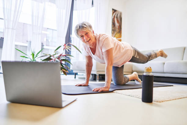 an 80-year-old senior citizen takes part in sports classes online and uses her laptop to train in her own living room - 80 year old imagens e fotografias de stock