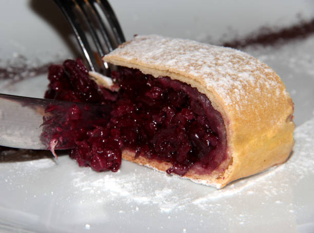 istock Cherry strudel on a white plate is cut. Use a fork and knife to cut strudel 1295982811