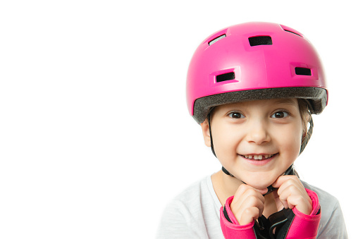 Toddler is wearing a pink helmet and wrist protection and is looking at camera on pure white background. She is about to learn skating