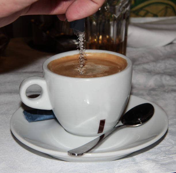 istock White Cup of coffee. Sugar is poured into the coffee drink. 1295984183