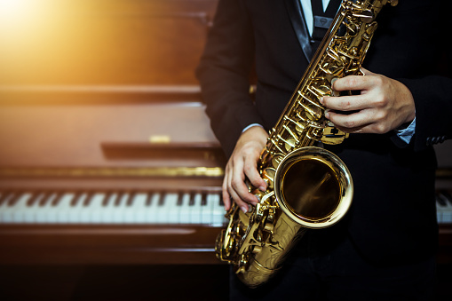 close up of Young Saxophone Player hands  playing alto sax musical instrument over piano  background  ,  closeup with copy space, vintage tone,  can be used for music background