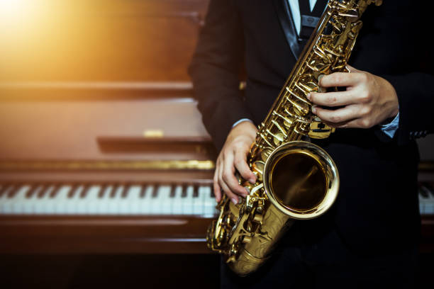 close up of Young Saxophone Player hands  playing alto sax musical instrument over piano  background stock photo