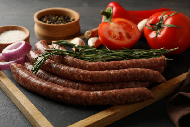 istock Board with raw sausages, herbs and spices on dark background 1295985676