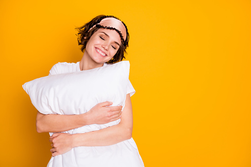 Close-up portrait of her she nice attractive lovely pretty cute glad dreamy, cheery brown-haired girl holding in hands cosy pillow isolated on bright vivid shine vibrant yellow color background