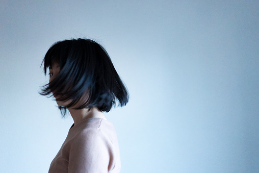 Portrait of Asian woman shaking her head and throwing her hair.
A woman turns around and her hair is hidden in her face.
Mysterious atmosphere. Momentary photo.
A photo in motion. Her hair is blurred.