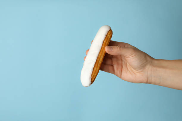 istock Female hand hold tasty eclair on blue background 1295988856