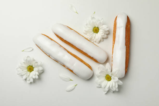 Delicious eclairs with custard and chamomiles on white background