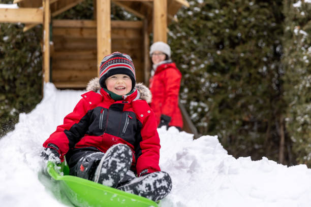 маленький мальчик санях на снегу на открытом воздухе в зимний период со своей матерью - little boys sled clothing slide стоковые фото и изображения