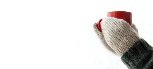 hands in knitted mittens hold a red mug