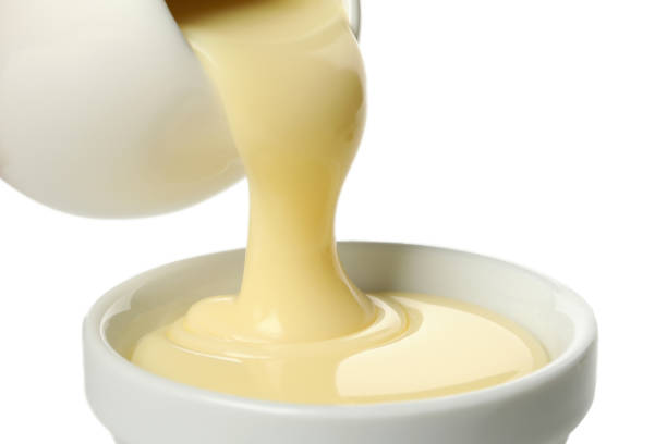 istock Condensed milk pouring in bowl, isolated on white background 1295992597