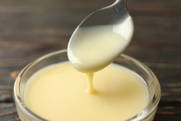 istock Spoon and bowl with condensed milk on wooden background 1295993321