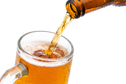 Close up view of a green bottle pouring beer to a glass shot against white background. The bottle and the glass are cold and condensation drops are visible on them. High resolution studio digital capture taken with Sony A7rII and Sony FE 90mm f2.8 macro G OSS lens