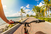 POV Point of view shot of a young sport man riding a bicycle in front of a paradise blue sea landscape over a brick pathway bicycle line at Key Biscayne, Miami Beach, Miami, South Florida, United States of America - USA