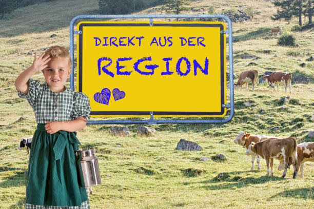 Little child in a dirndl with a milk jug in her hand in front of an alpine meadow with cows and the sign \