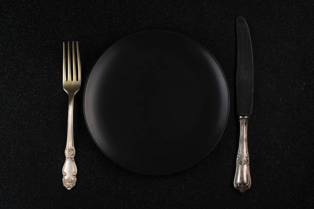 istock Black plate, fork and knife on a black table. View from above. 1295997526