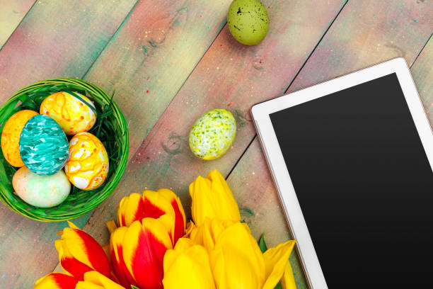 istock tablet screen for message and colorful tulips and easter eggs on wooden background 1295997545