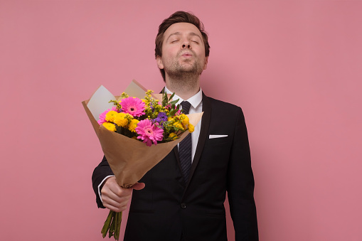 Young smiling man holding a bouquet of flowers making a proposal.