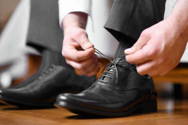 Man tying shoelaces on black shoes Businessman tying shoelaces on classic elegant black leather shoes, or groom dressing in preparation for wedding day. Close-up shot from the side lace up stock pictures, royalty-free photos & images