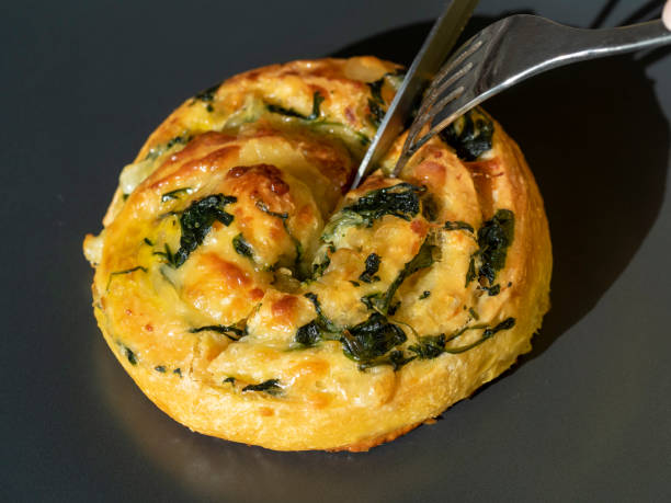 Pastry with spinach and cheese is cut with a knife and fork. Side view, close-up