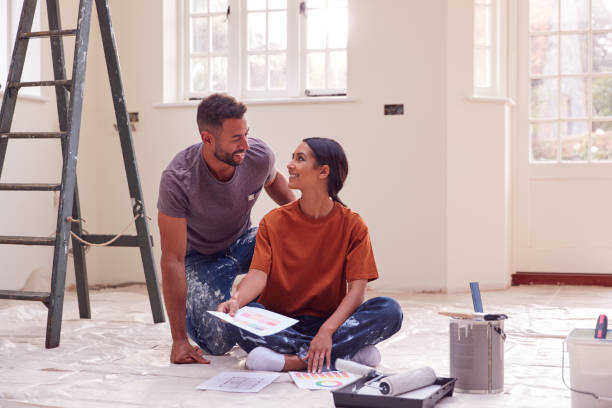 couple sitting on floor with paint chart ready to decorate new home - home improvement imagens e fotografias de stock