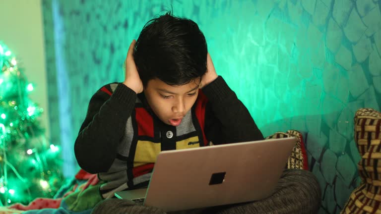 Boy using laptop sitting on bed