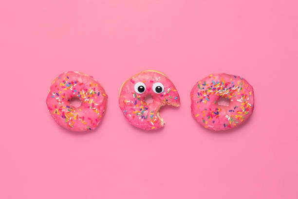 istock Three pink glazed donuts on pink with googly eyes 1296010011