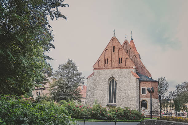 View of old stone Roman Catholic Parish of the Holy Cross. Building with orange brick roof, arcade window and blooming tea rose bush on a sunny autumn day in Krakow, Poland.