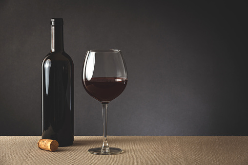 Glass and bottle of red wine standing on a light brown tablecloth, grey background