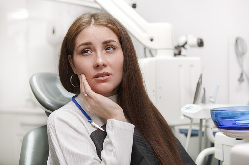 Close up of a woman suffering from toothache, sitting in dental chair at the clinic