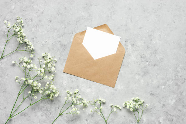istock Blank card mockup in a craft envelope and hispophila flowers. Gray concrete grunge background. Spring greeting template. Flower composition. Top view, flat lay. 1296013765
