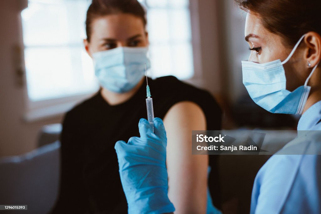 Nurse giving vaccine to young woman during COVID-19 season. Nurse in scrubs prepared to get vaccinated patient in hospital against flu and measles during an epidemic. Flu shot, protection and prevention of viral infectious diseases. 25-29 Years Stock Photo
