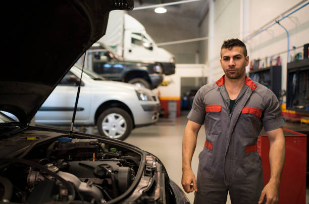 Young uniformed mechanic poses next to a vehicle in a workshop