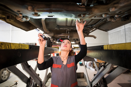 mechanic woman checks the underside of an industrial car, its chassis and axles on a lifting bench.