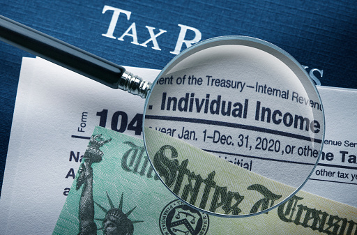 A magnifying glass on top of an IRS 1040 form and a U.S. Treasury refund check.