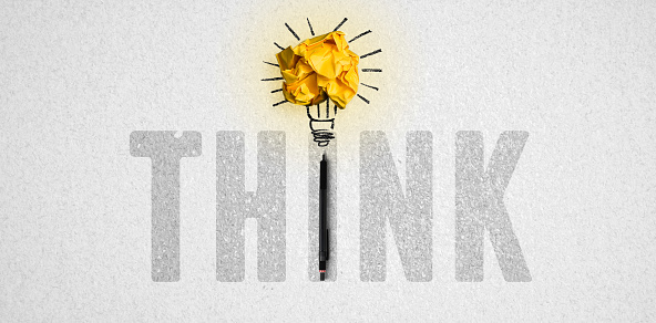 message THINK and crumpled paper forming a lightbulb symbol on paper background