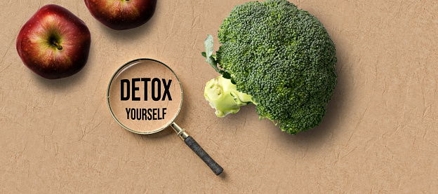 a magnifying glass with message DETOX and broccoli and apple on paper background