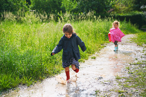 Children having fun in a puddle on a sunny day. Two girls running.