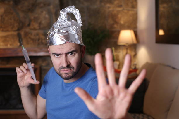 Man wearing tin foil hat holding syringe Man wearing tin foil hat holding syringe. anti vaccination stock pictures, royalty-free photos & images