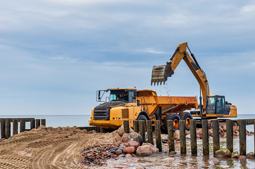 Industrial truck loader excavator moving sand and unloading it into a dumper truck